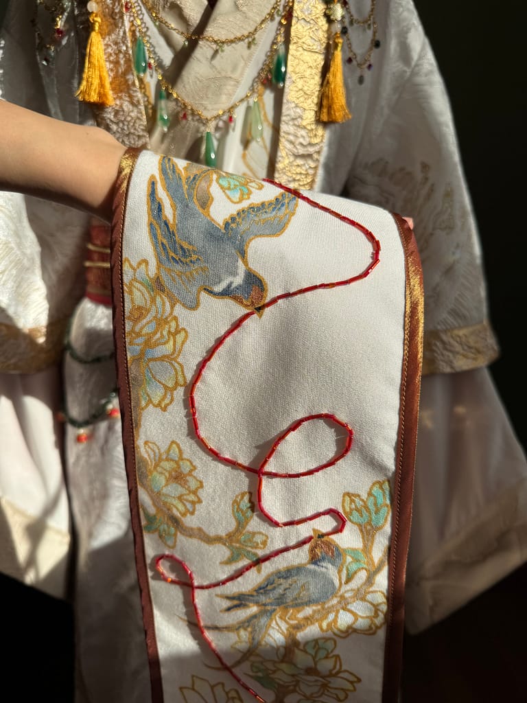 Ilia is holding their hand-painted bixi featuring two house sparrows sitting on gardenia branches and holding the red thread of fate to symbolize Hua Cheng and Xie Lian’s connection.