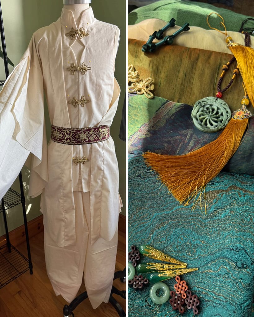 On the left is a patterning mockup of a Kong Hongjun cosplay featuring a vest, jacket with layered flowing sleeves, and trousers. On the right is a variety of brocade and silk fabrics, beads, and sewing notions to be used in constructing the cosplay.